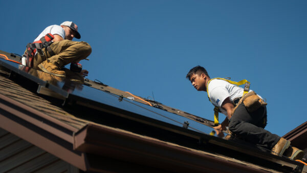 Suncovia solar installers working on a residential roof in Massachusetts, installing solar panels to reduce electricity costs.