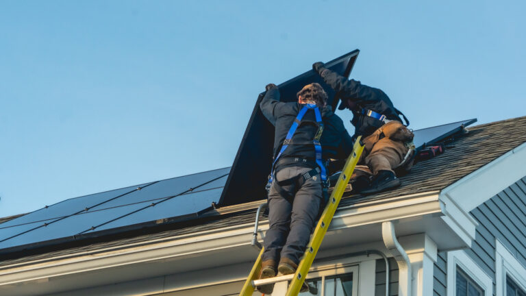 two workers holding solar panels on top of shingles roof