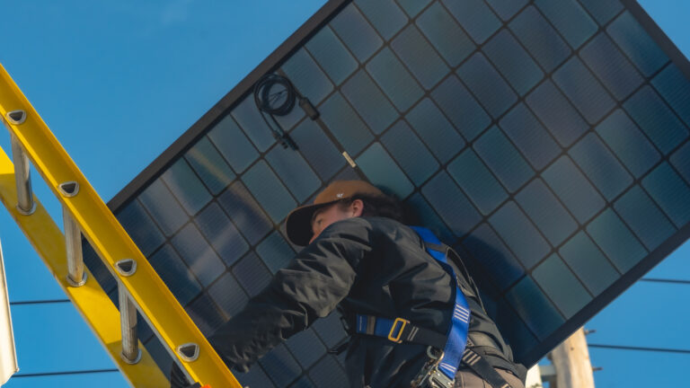 worker carrying solar panel on ladder